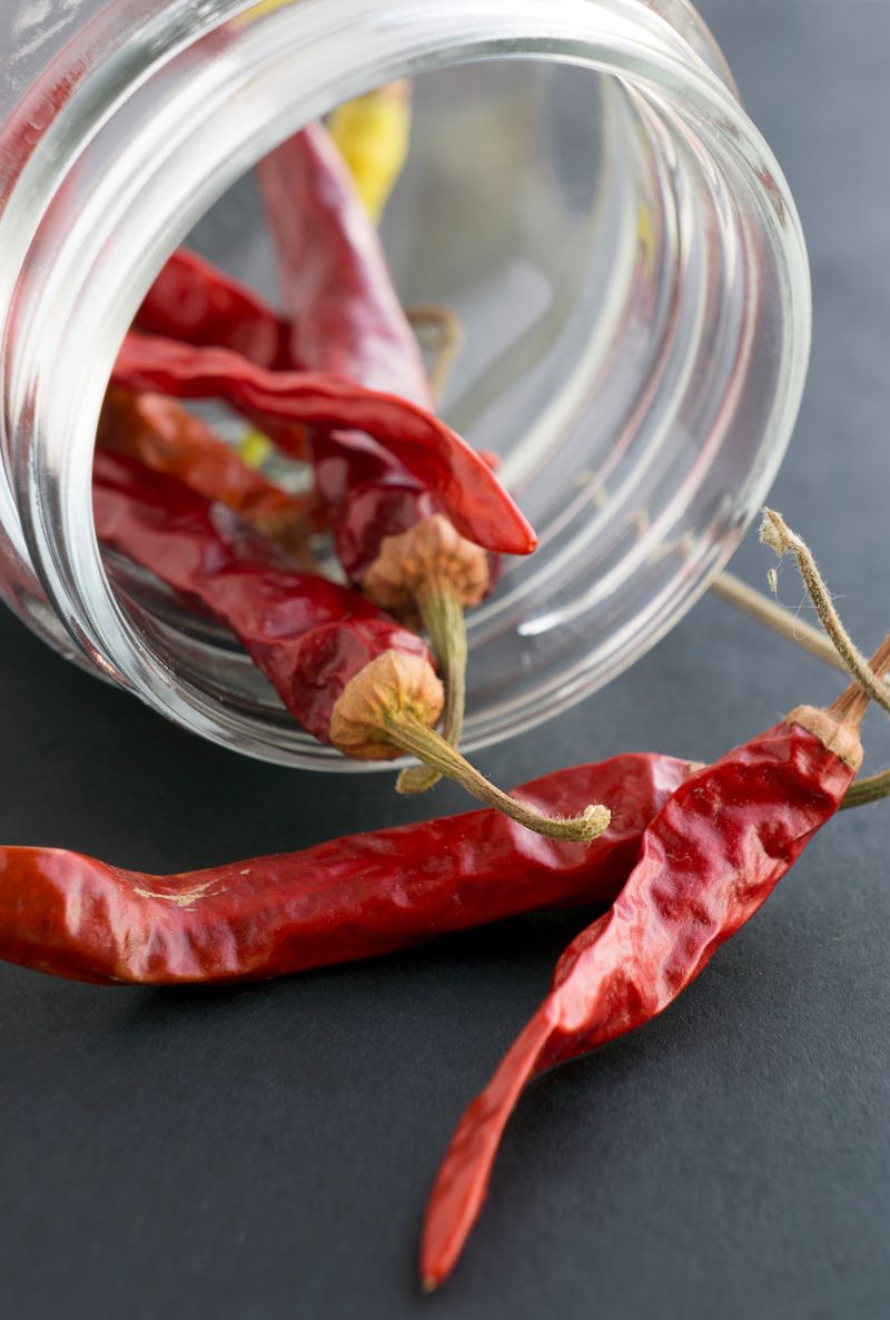 Dried red chile peppers spilling from a glass bowl onto a dark surface.
