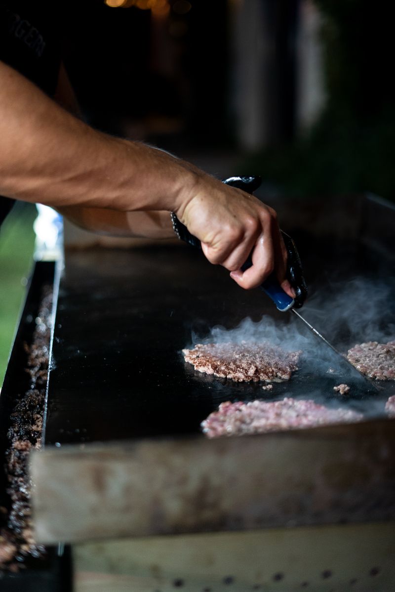 Cook pressing a smash burger on a flat-top griddle with smoke rising.