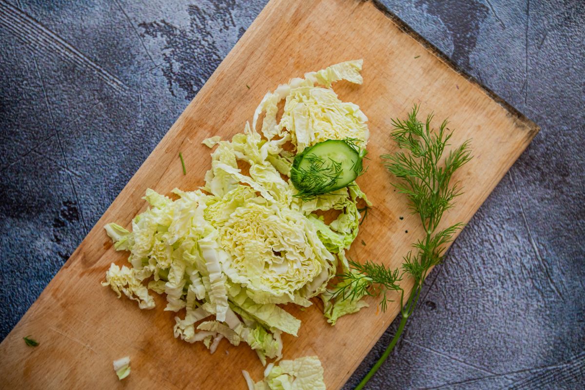 Shredded cabbage on a wooden cutting board with herbs.